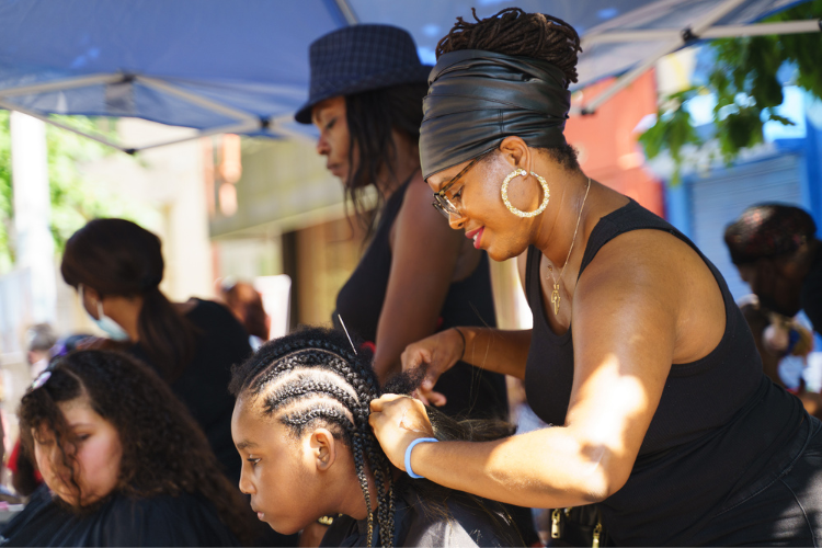 A girl gets her hair braided by a volunteer hairstylist at the back-to-school event in West Harlem. The hair braiding was provided at no cost and was one of many free resources at the annual event. Photo Credit: Henry Danner