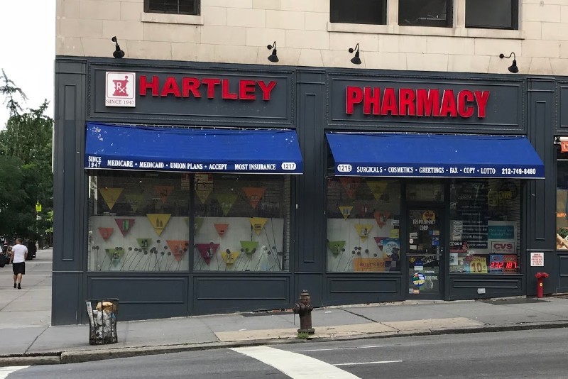 A gray storefront with a neon sign saying "Harley Pharmacy" above a blue awning.