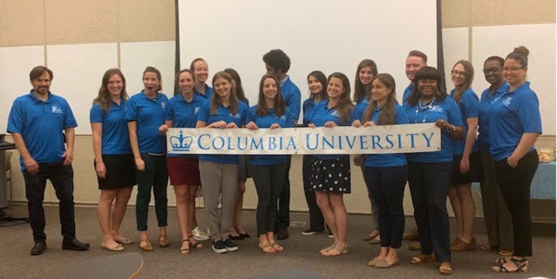 A group of adults in blue polo shirts holding a Columbia University banner.