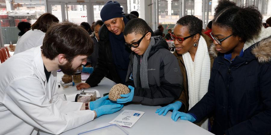 A scientist in a white coat shows a two children and two adults a model of a brain.