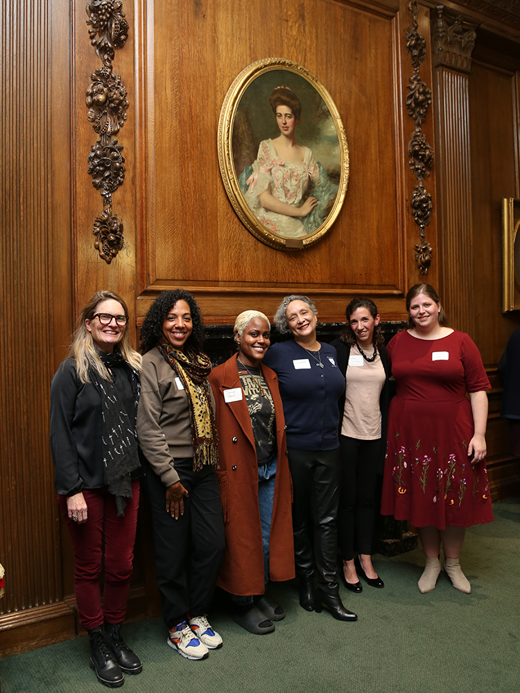 Six people, including four Bundles Scholars, stand in front of the fireplace in Low Library's Burden Room. 