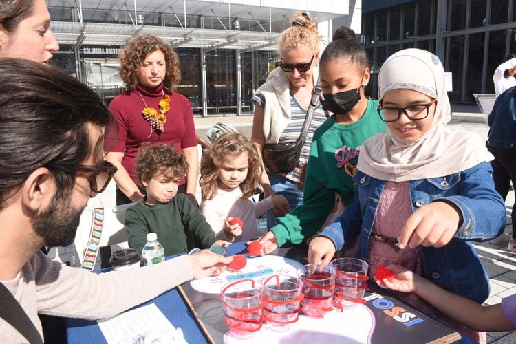 A bunch of kids surround a Saturday Science Table in the square on the Manhattanville campus. 