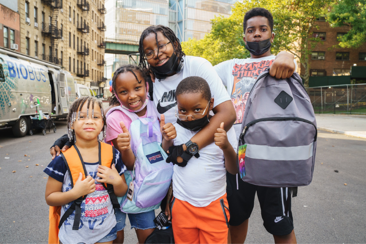 Five kids at a backpack drive in Uptown New York posing for a photo. 