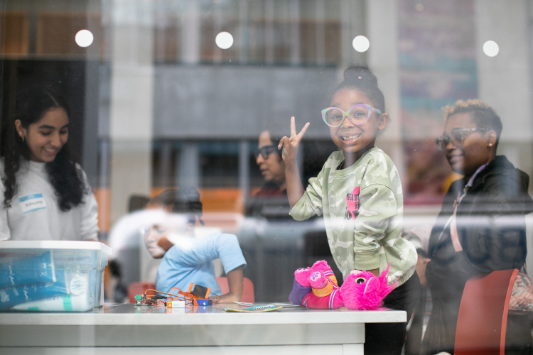 A Saturday Science participant rocks a peace sign during science activities in the Zuckerman Institute's Education Lab on Columbia's Manhattanville campus. Photo by David Dini. Saturday Science participants wave a peace sign during Manhattanville Community Day in October 2023.