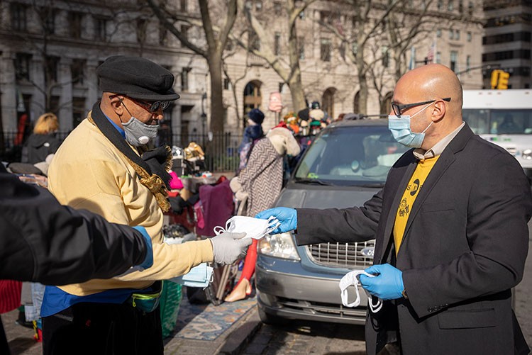 Man hands out a mask to another man on a New York City street.