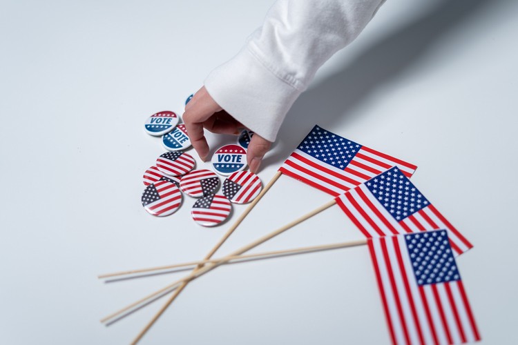 A hand reaching for a vote pin among a pile of american flag pins and flags.