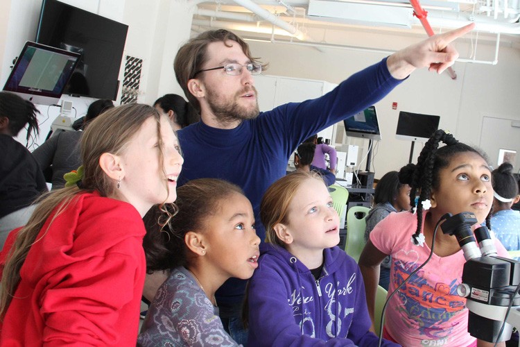 Teacher pointing at something outside the frame with a group of students.