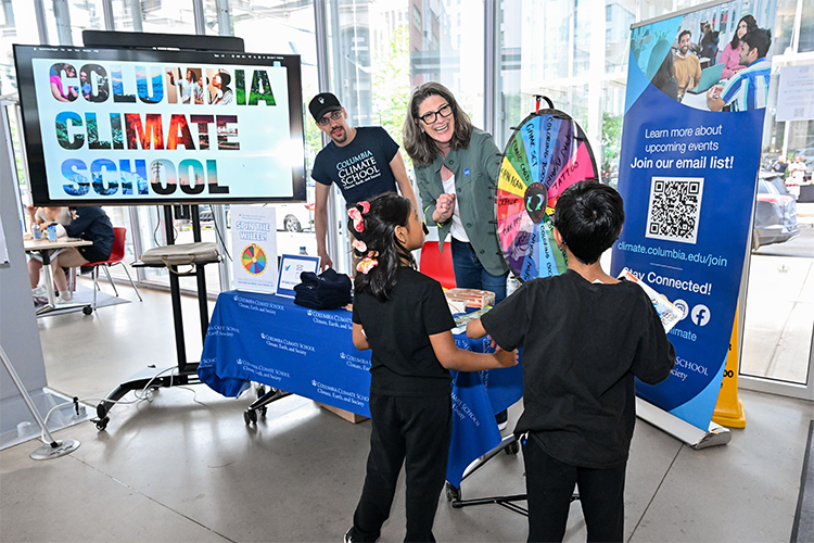 Two young guests spin the wheel at Columbia Climate School's table. Photo by Diane Bondareff. Two kids spin a wheel at a table staffed by two Columbia Climate School employees.