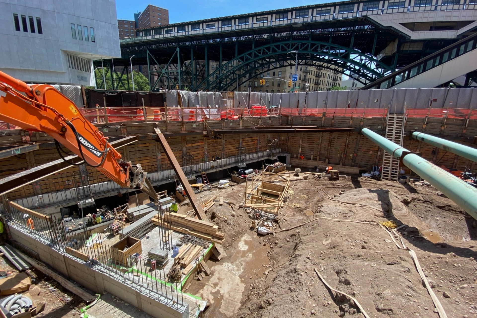 A view of the 600 W. 125th Street construction site with steel beams running across a dirt pit abd the elevated 1 train station in the background.