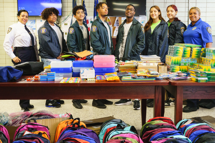 Deputy Inspector Alexandra Sarubbi, Detective Johanna Ureña and youth from the 26th Precincts NYPD Explorers program after a long day of unpacking and sorting supplies for the annual back-to-school event. Photo Credit: Henry Danner