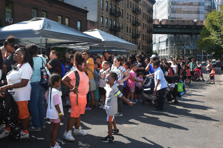 A backpack distribution line wraps around Old Broadway. Hundreds of Uptown families are supported annually through the event in West Harlem. Photo credit: Susan Farley. A backpack distribution line wraps around Old Broadway. Hundreds of Uptown families are supported annually through the event in West Harlem. Photo credit: Susan Farley