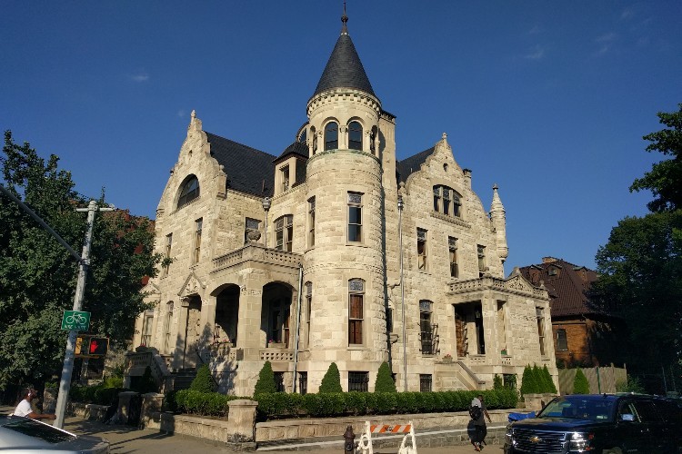 A large white stone mansion behind a row of low hedges against a blue sky