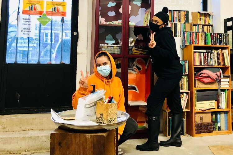 Two women in masks in a book store, making the peace sign. 