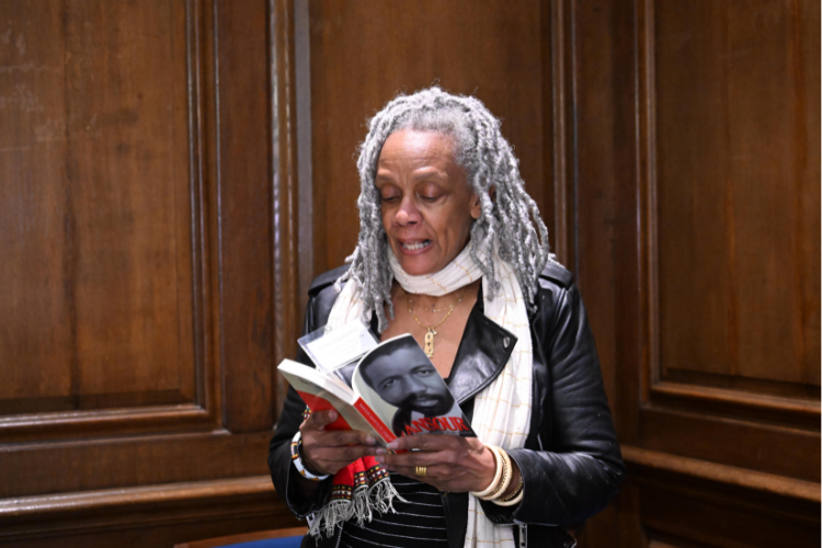 Bonita LloydNettles, a Bundles Scholar from the 11th cohort, shares a poetry reading at the reception. Photo by Eileen Barroso. A woman reads from a book facing the crowd.