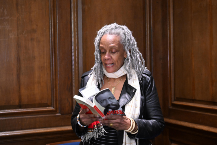 A woman reads from a book facing the crowd. 