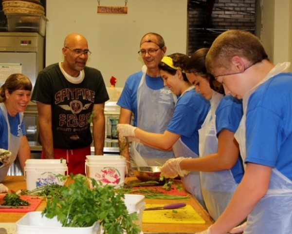 Six people around a large counter preparing food on cutting boards.