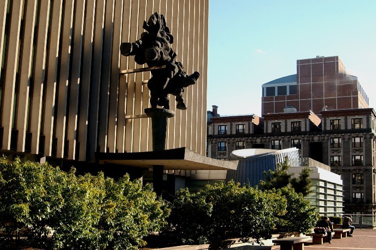 Benches and plants in front of a large concrete building with a statue in front of it.