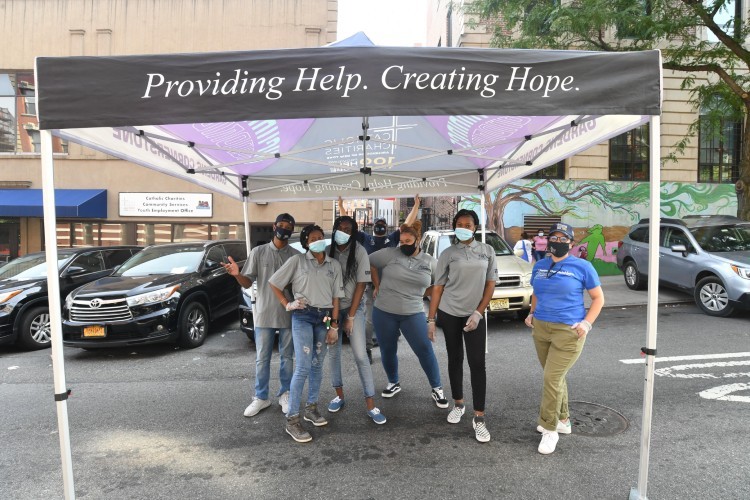 A group of young adults under a tent that says "Providing Help. Creating Hope"