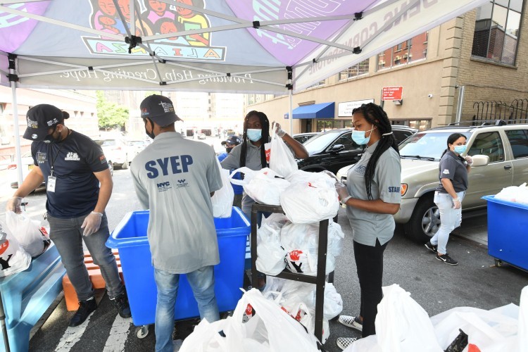 A group of people removing plastic bags from a rolling bin.