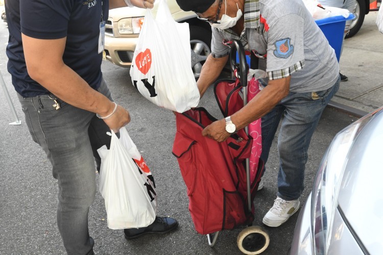 Photo credit: Eileen Barroso. One person puts a bag of food in another person's fabric cart.