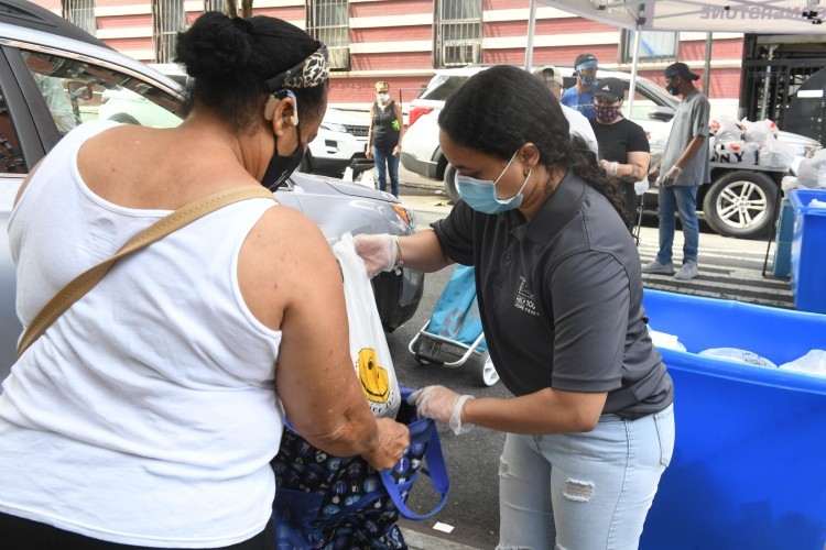 Photo credit: Eileen Barroso. A woman puts a plastic bag of food into the bag that another woman is holding open.