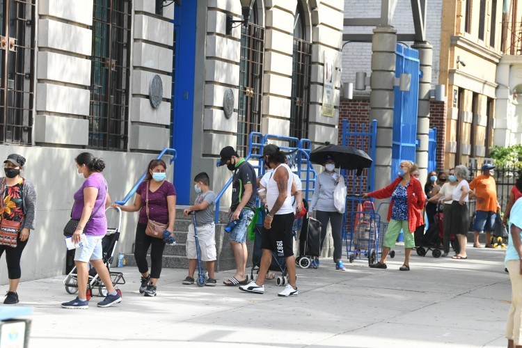 A line of masked people on the sidewalk.