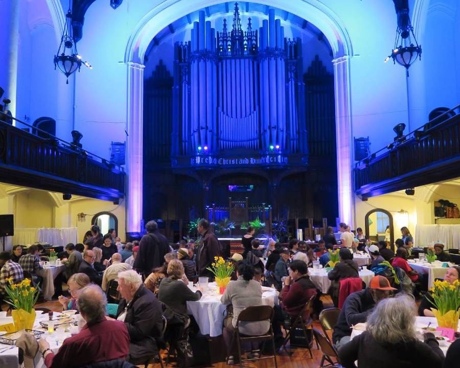 People eating a meal at tables in a church, with the church organ in the background.