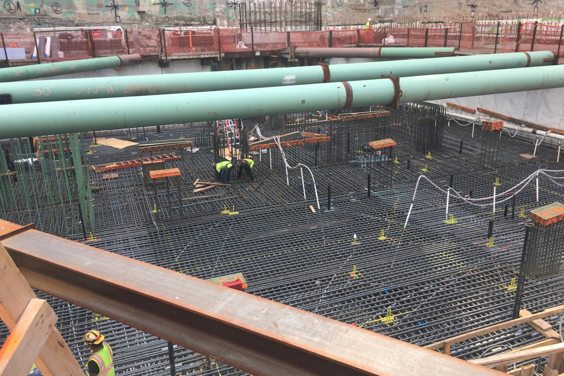 An view of the 600 W. 125th Street construction site facing south, with thousands of rebar placed on the ground and large green pipes running overhead.