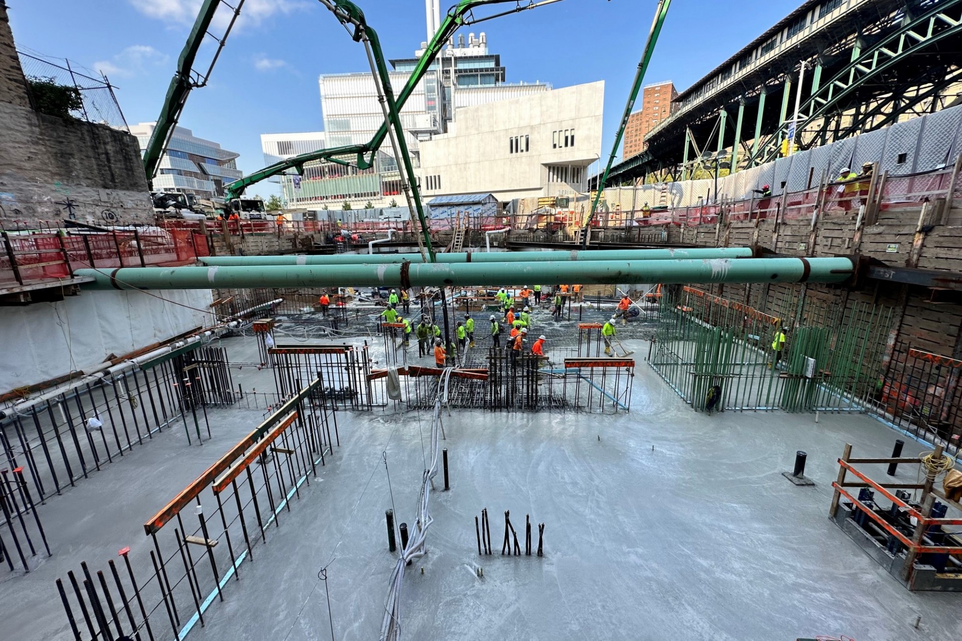 A view of the northern part of the 600 W. 125th Street construction site, with rebar sticking out of concrete on the ground and large green pipes running overhead.