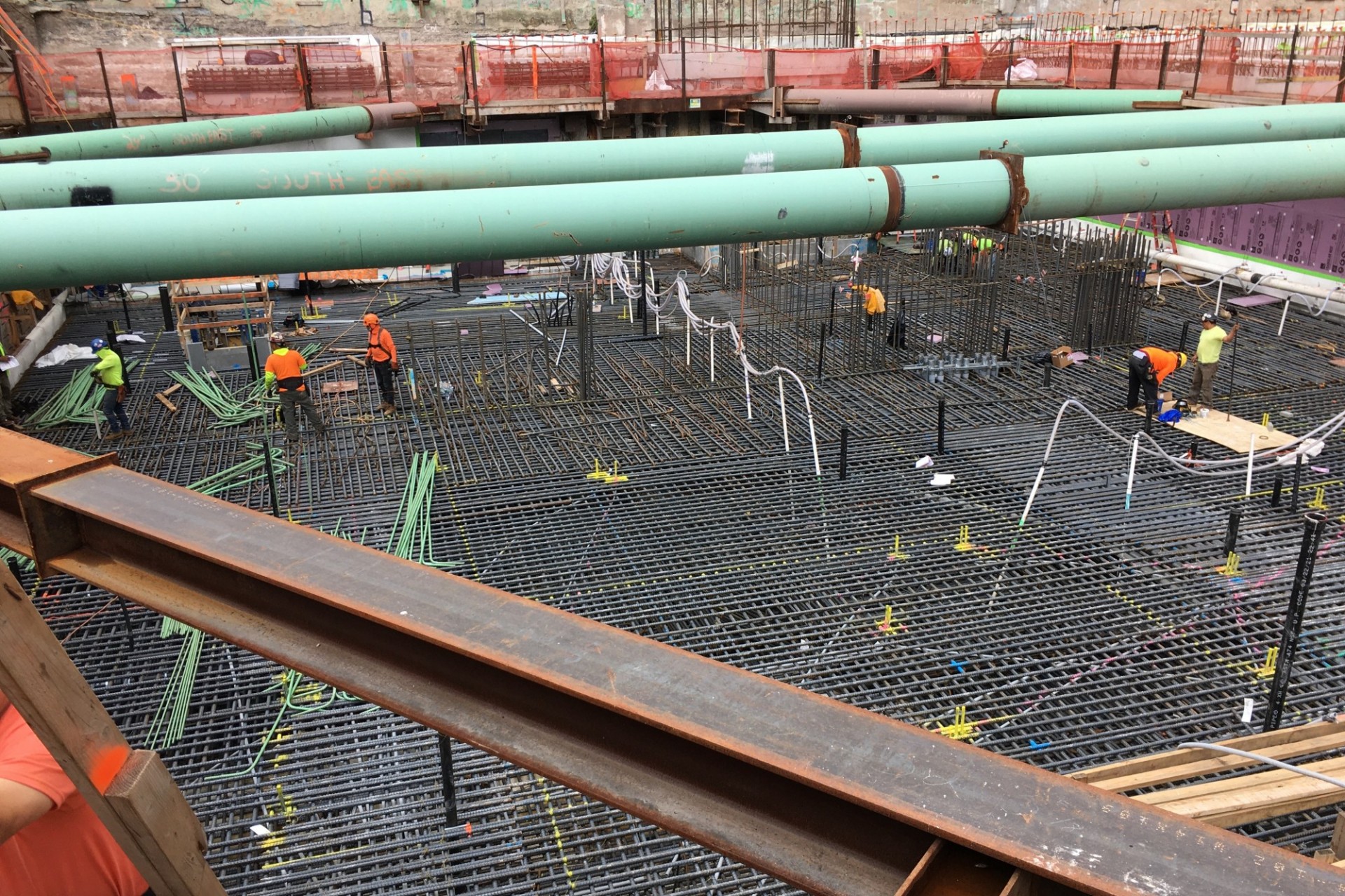 A view of the southern part of the 600 W. 125th Street construction site, with thousands of rebar placed on the ground and large green pipes running overhead.