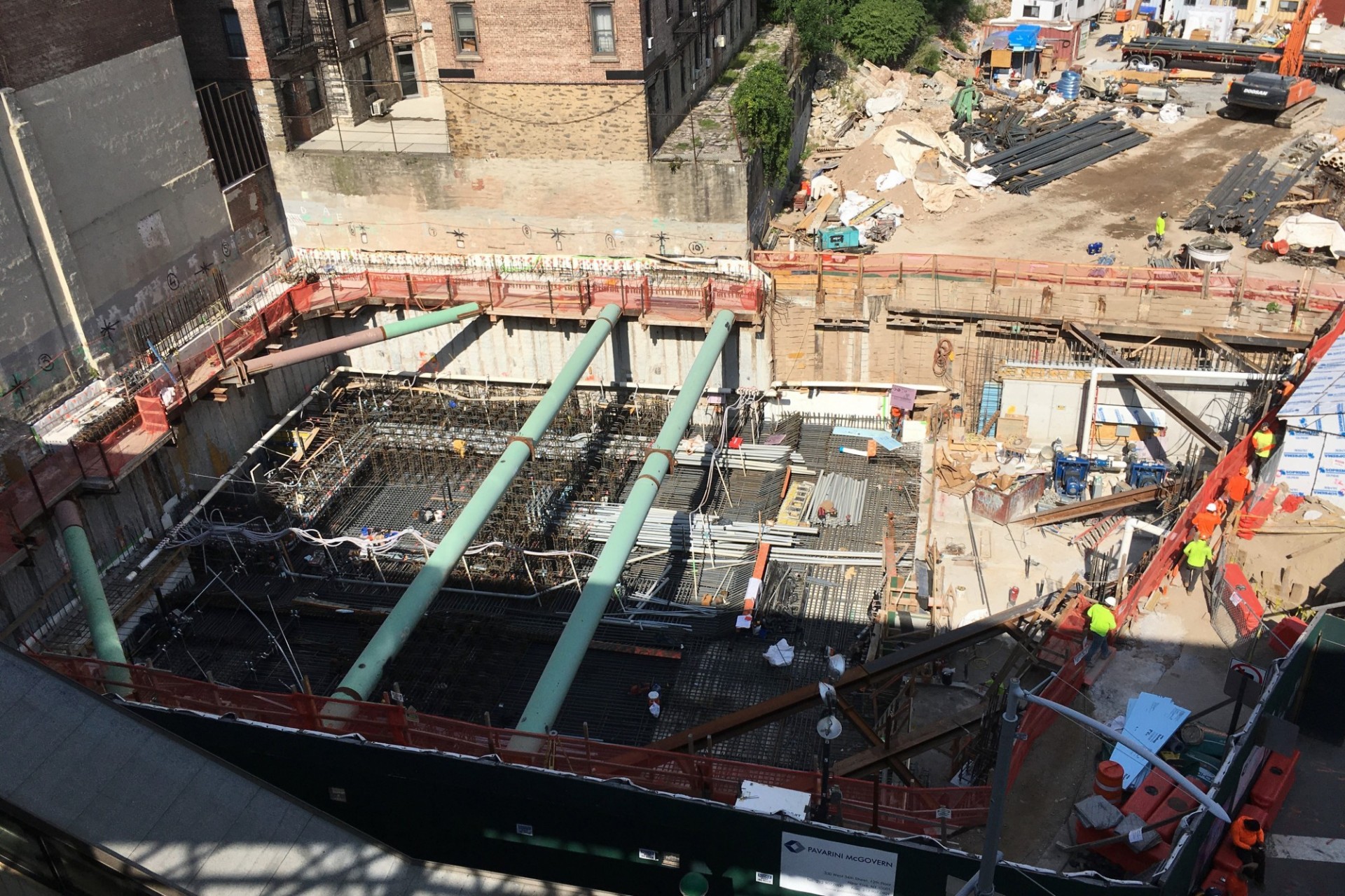 An aerial view of the 600 W. 125th Street construction site, with rebar covering half of the site, green pipes overhead, and equipment on the other half to perform foundation work. 