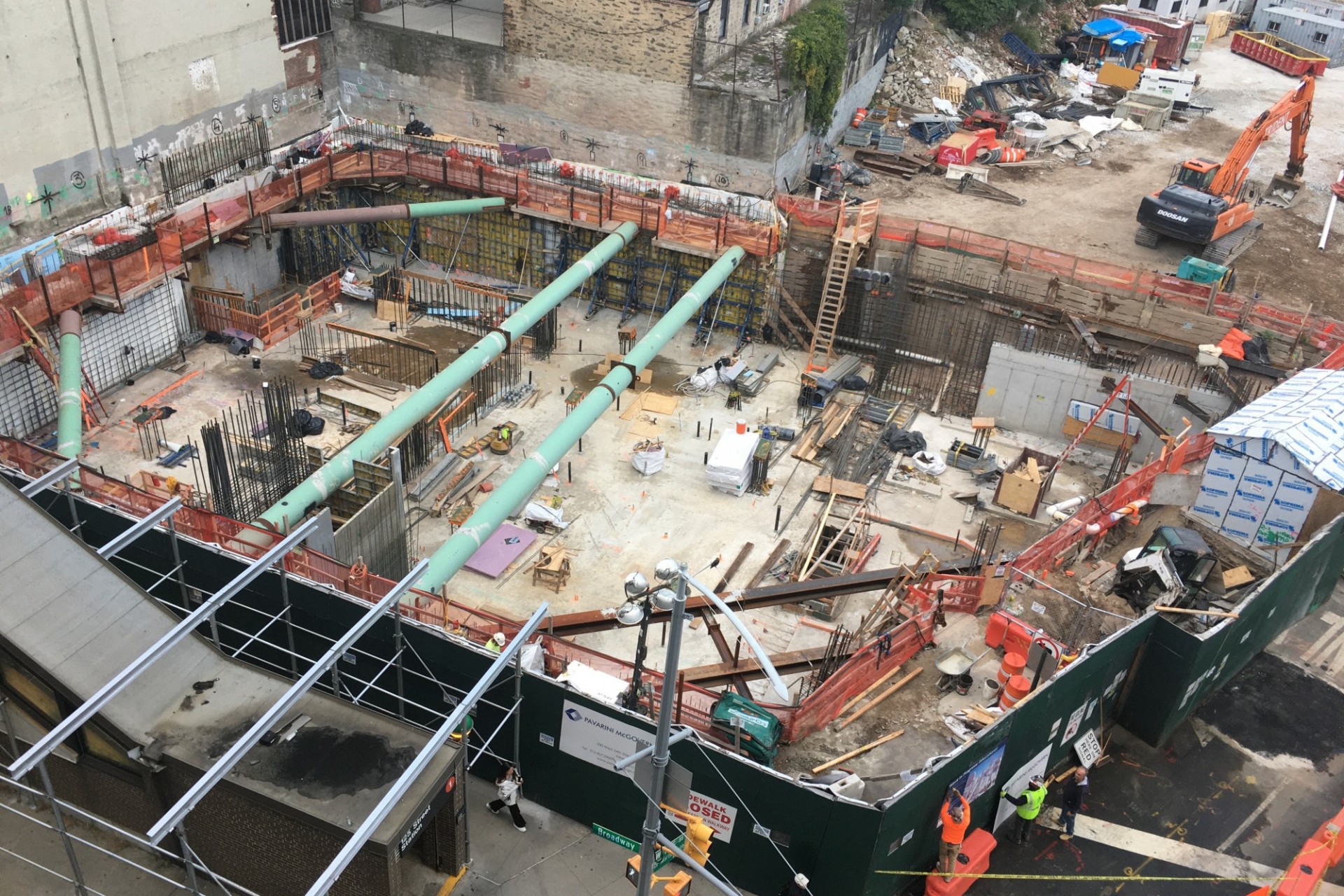 A aerial view of the 600 W. 125th Street construction site, full of materials and large green pipes running overhead.  ﻿