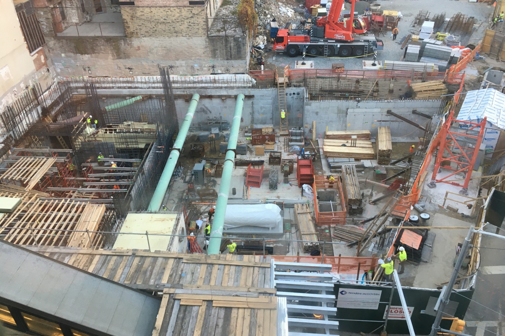 A aerial view of the 600 W. 125th Street construction site, full of materials and large green pipes running overhead. 