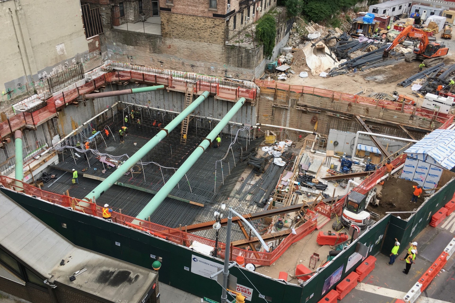 An aerial view of the 600 W. 125th Street construction site, with rebar covering half of the site, green pipes overhead, and equipment on the other half to perform foundation work.