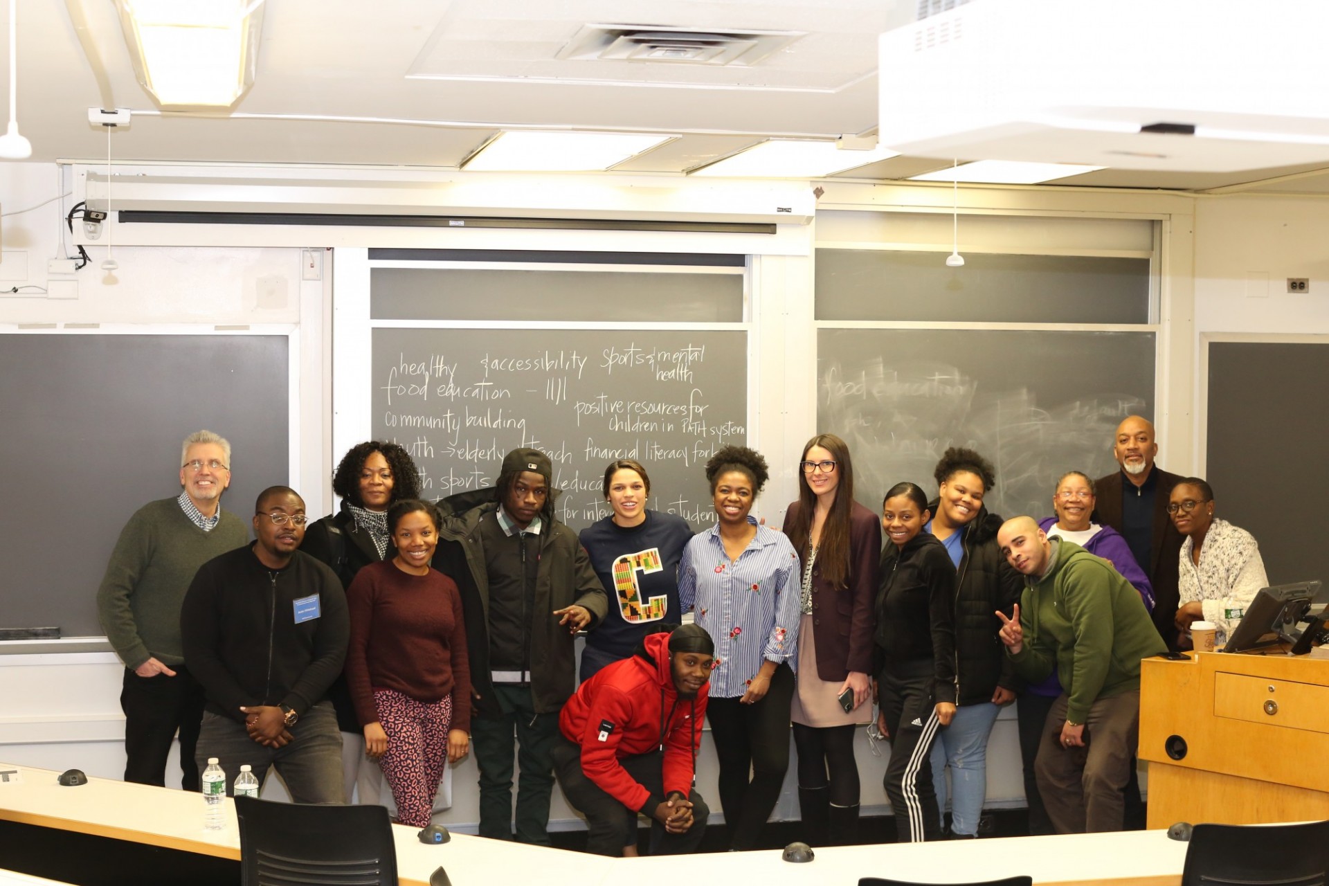 A group of people of stand in front of a blackboard in a classroom.