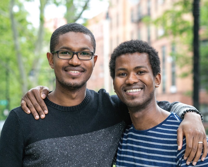 Two brothers smiling and posing for the camera outside.