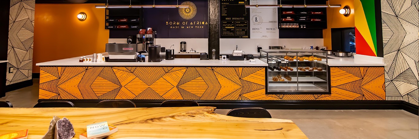 The counter of a cafe, with a pastry case to the right and a sign saying "Born of Africa" behind the counter.