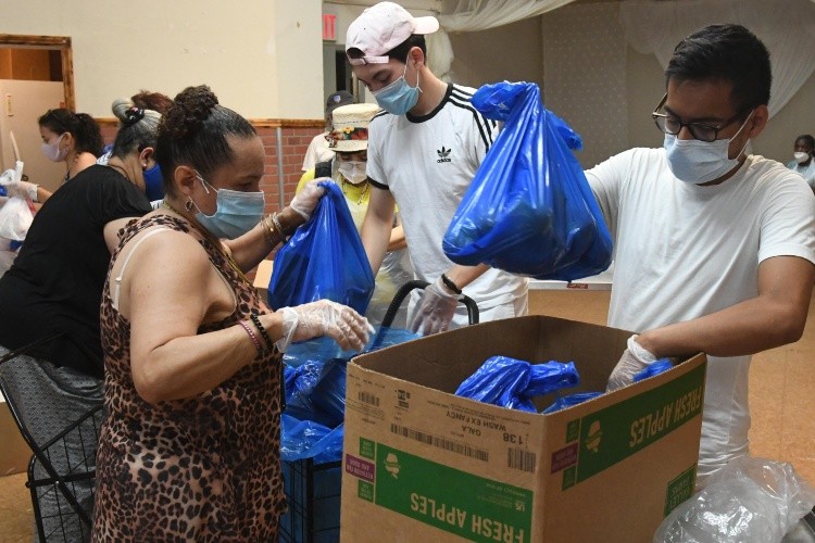 Masked men and women put bags of food into boxes.