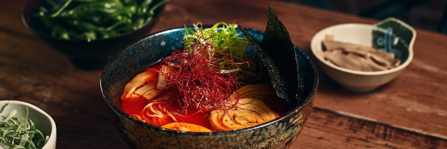A bowl full of red broth with seaweed sheets, meat, and other toppings.