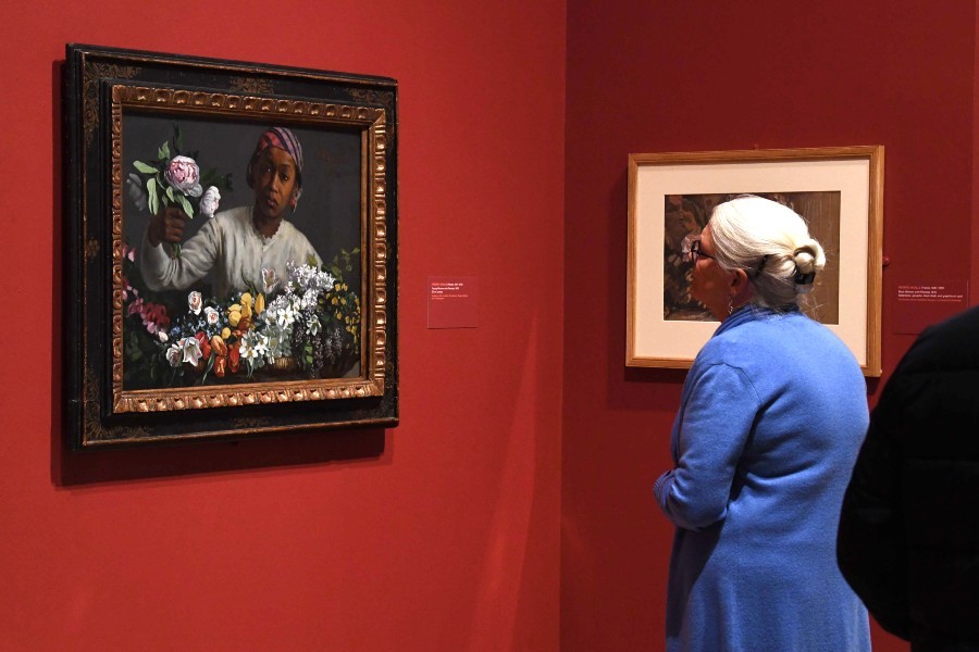 A white-haired woman looks at a painting of a black woman arranging flowers as part of the Posing Modernity exhibition at the Wallach Gallery.