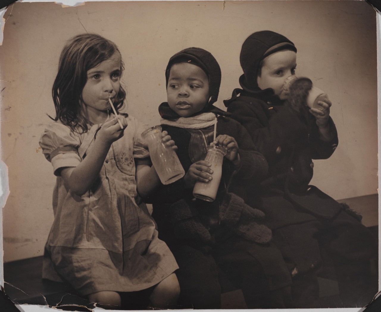 Children in East Harlem, Union Settlement House, ca. 1940 Three young children drinking milk from a glass bottle and straw.