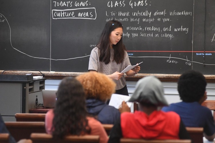 Instructor in front of chalk board with back of students heads facing instructor