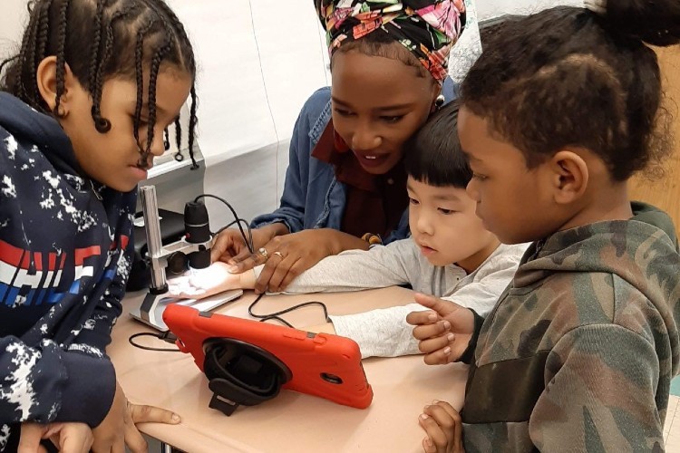 Three children and an adult women grouped together looking at a tablet screen.