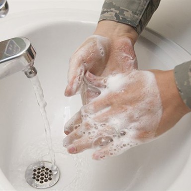 A person washes their hands with soap beneath of running faucet.