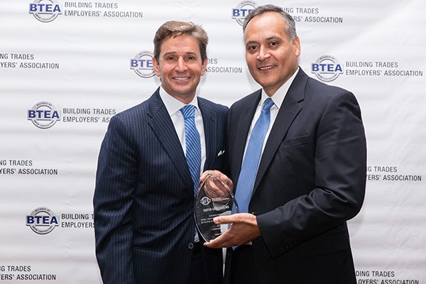 Two men holding a glass award in front of a Building Trades Employers' Association background.