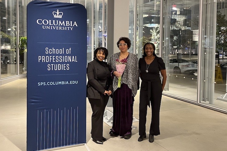 A Columbia University School of Professional Studies sign and three women smiling at the camera.
