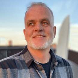 A man poses for a photo on top of a building roof. 