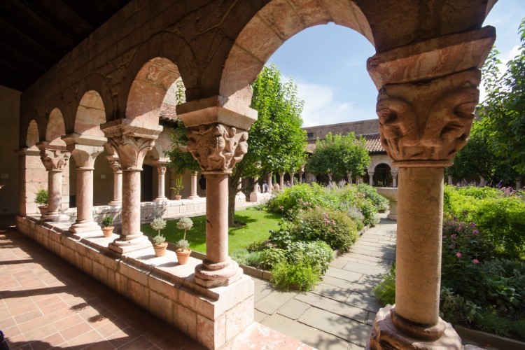 One of the gardens at the Met Cloisters. A view of a garden through a walkway with stone arches.