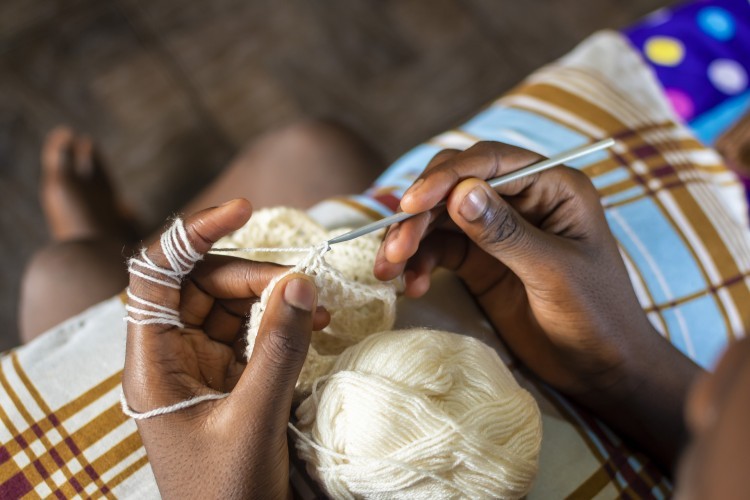 Young person's hands crocheting with cream colored yarn.