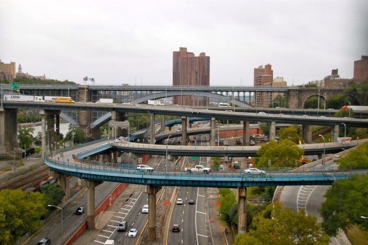 A highway interchange in the Bronx with high rise buildings and a bridge in the background.
